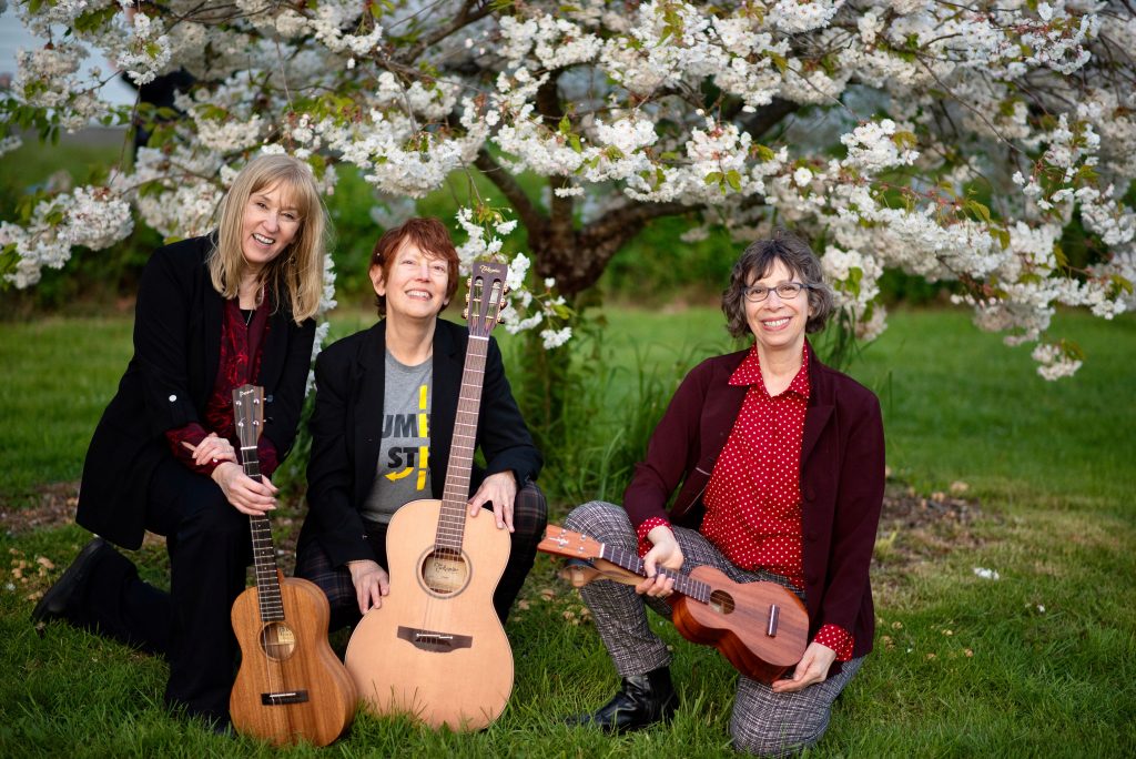 Patrice O'Neill, Kathleen Tracy and Arni Adler kneeling with their instruments under a blooming cherry tree in Discovery Park, Washington.