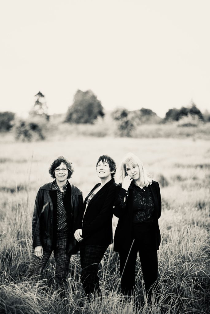 Arni Adler, Kathleen Tracy and Patrice O'Neill standing in a field in Discovery Park, Seattle Washington.